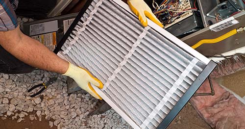 Image: a man changing out an HVAC air filter.
