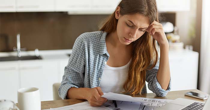 Image: a woman looking over her bills wondering how to fit in the cost of a replacing a furnace.