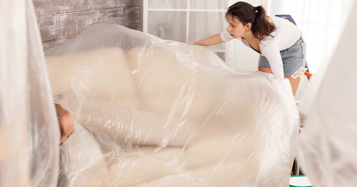 Image: woman covering her furniture with a plastic sheet. When you repipe a home you'll need to protect your furniture.