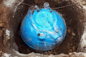 A blue water tank partially buried in the ground, wrapped in plastic and surrounded by soil.